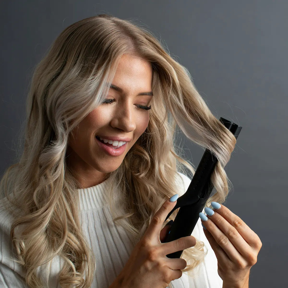 Blonde woman using a curling iron to style her hair, illustrating a common cause of hair heat damage