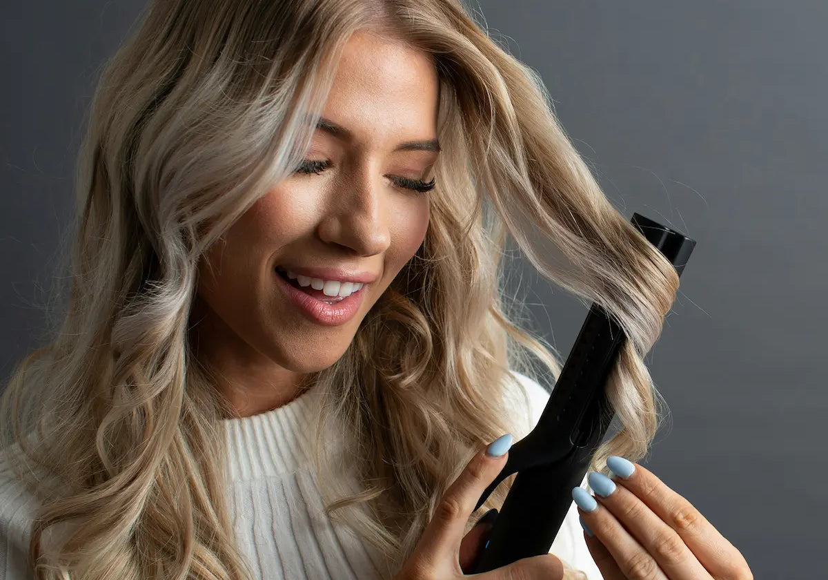 Blonde woman using a curling iron to style her hair, illustrating a common cause of hair heat damage