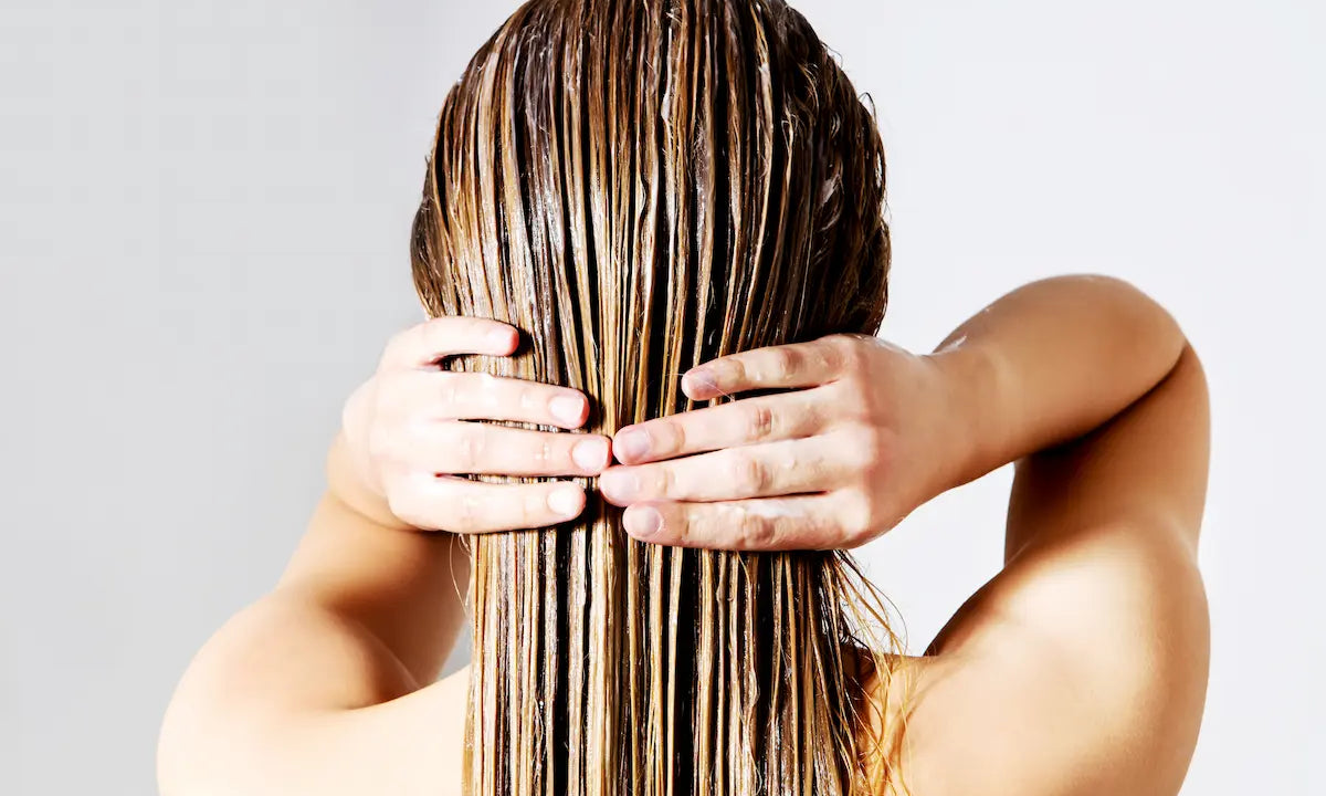Person applying hair conditioner evenly to the lengths of long wet hair