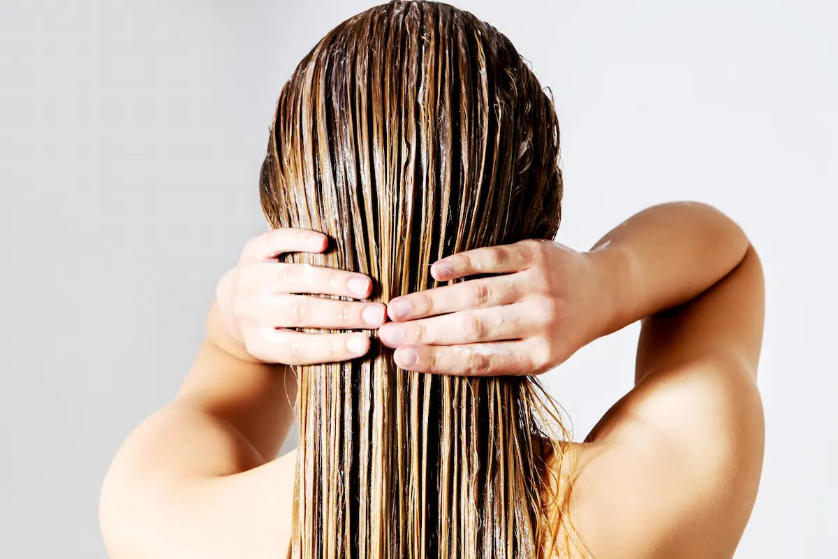 Person applying hair conditioner evenly to the lengths of long wet hair
