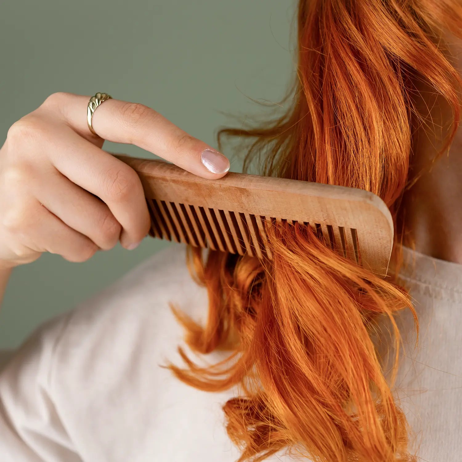 Person combing vibrant red hair with a wooden comb to check for seasonal summer hair shedding