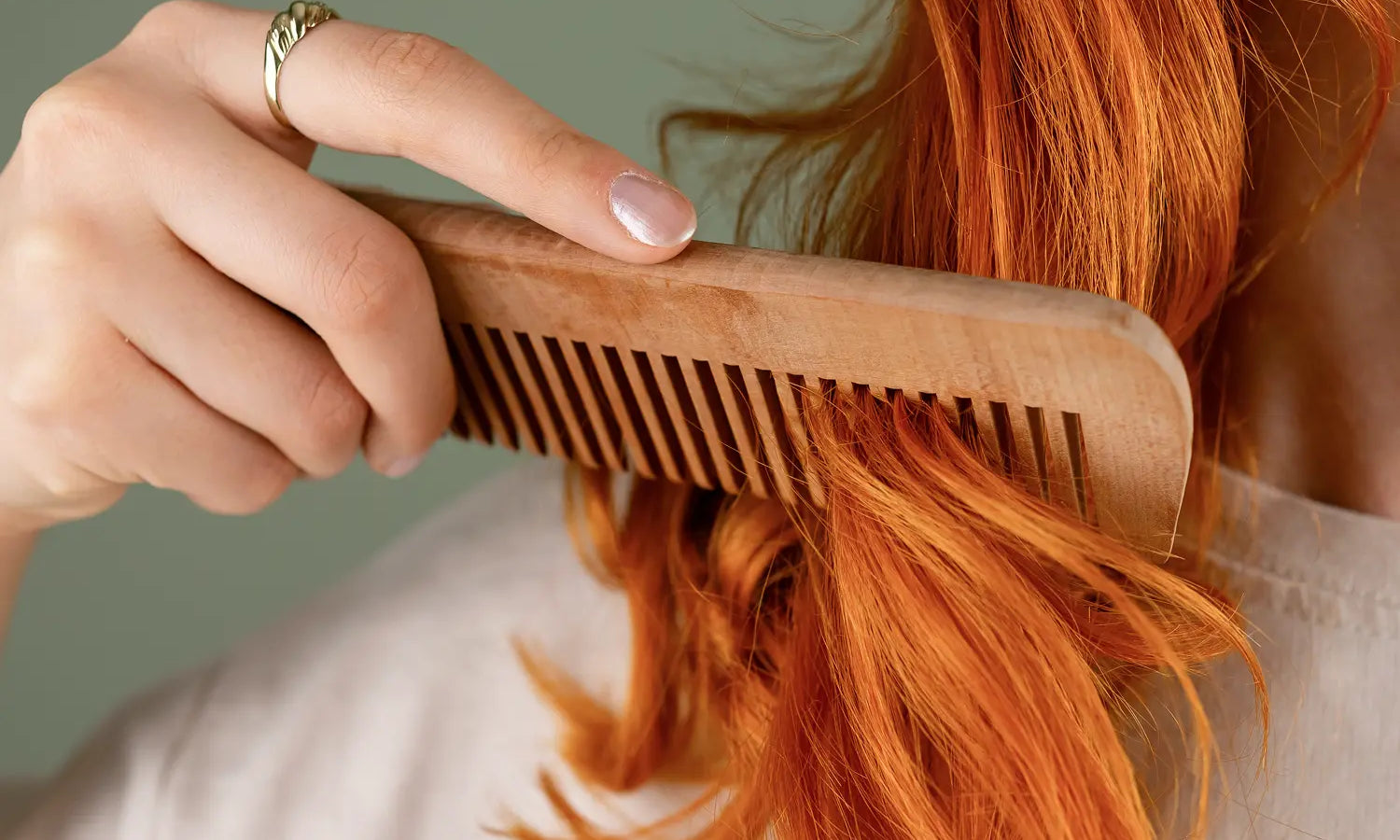 Person combing vibrant red hair with a wooden comb to check for seasonal summer hair shedding