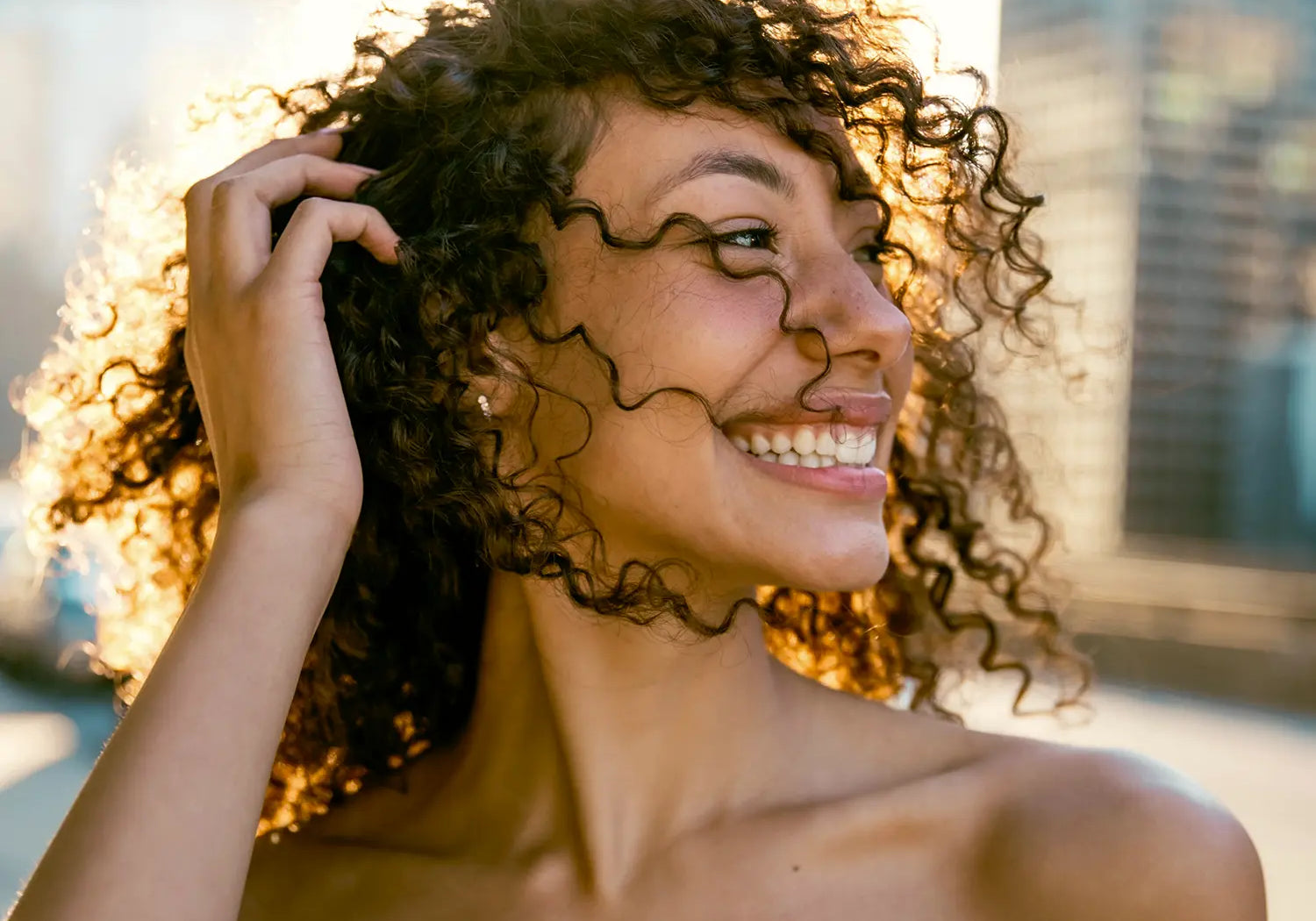 Smiling woman with defined, frizz-free curly hair in the summer sunshine