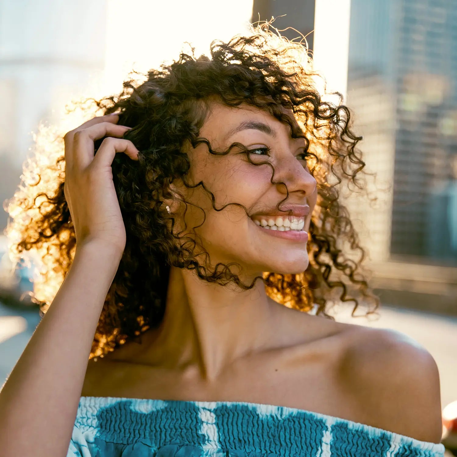 Smiling woman with defined, frizz-free curly hair in the summer sunshine