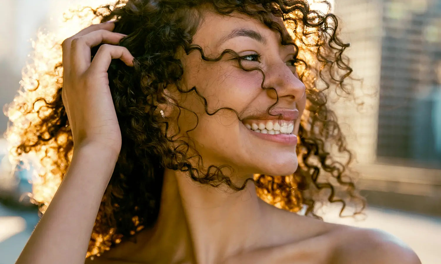 Smiling woman with defined, frizz-free curly hair in the summer sunshine