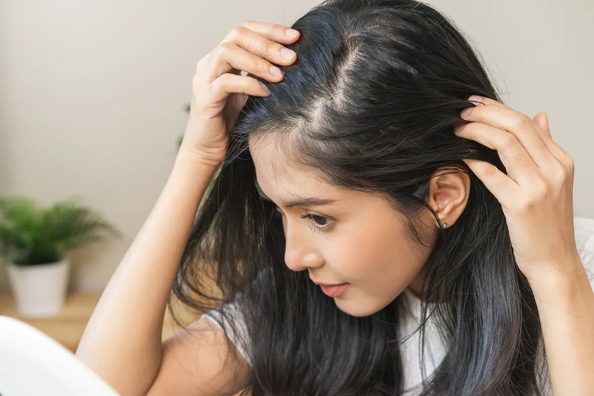  Woman looking in a mirror examining her hair parting for dry or oily scalp symptoms