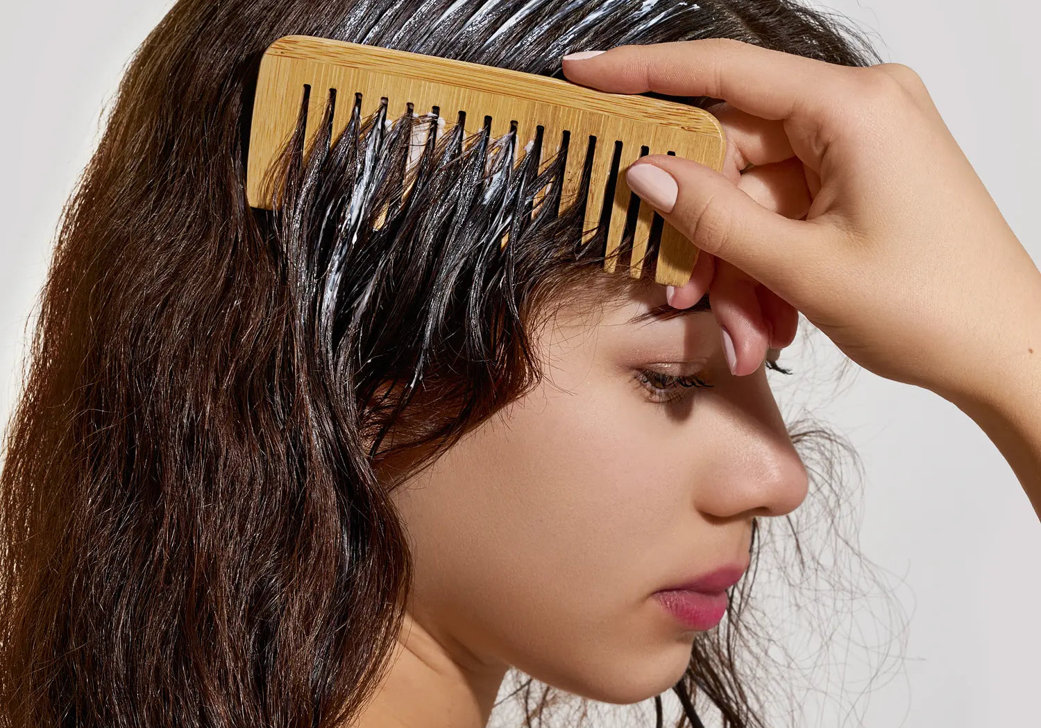 Woman using a wide-tooth wooden comb to evenly distribute deep conditioner through wet hair