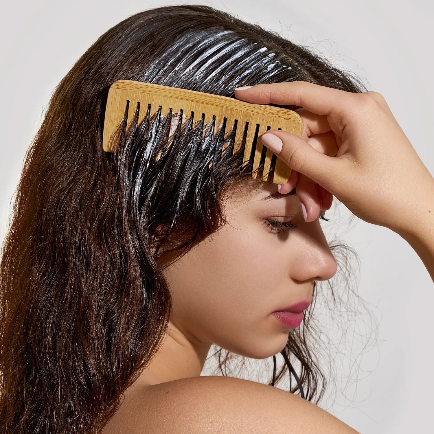 Woman using a wide-tooth wooden comb to evenly distribute deep conditioner through wet hair
