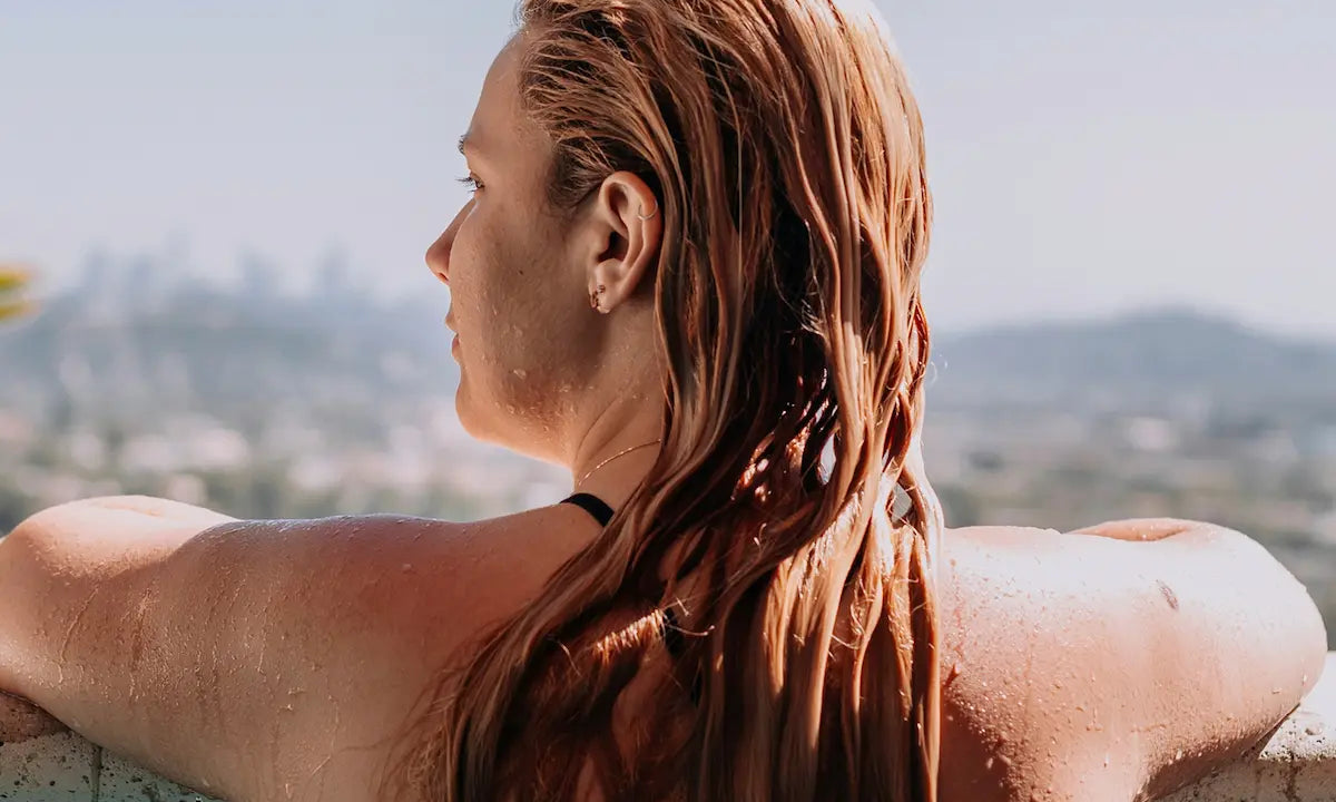 Woman with wet hair leaning on the edge of a swimming pool during summer