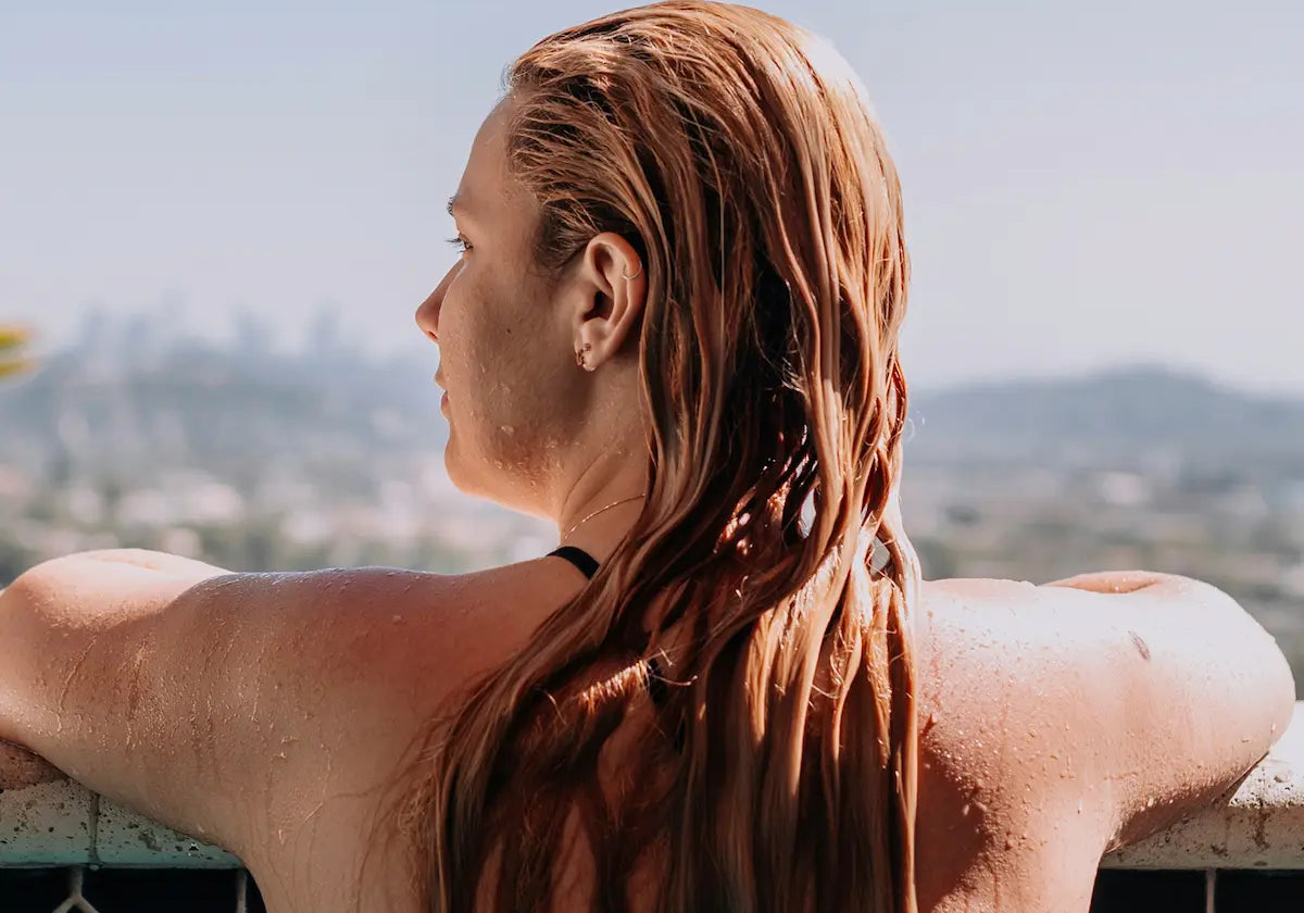 Woman with wet hair leaning on the edge of a swimming pool during summer